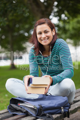 Cheerful casual student sitting on bench holding books Cheerful casual student sitting on bench holding books
