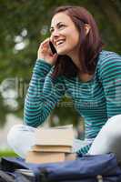 Cheerful casual student sitting on bench phoning