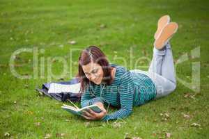 Happy casual student lying on grass reading