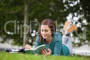 Calm casual student lying on grass reading