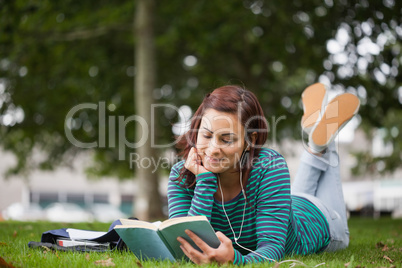 Smiling casual student lying on grass reading
