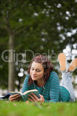 Attractive casual student lying on grass reading