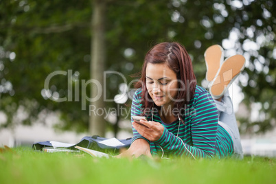 Attractive casual student lying on grass texting