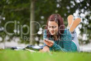 Attractive casual student lying on grass texting
