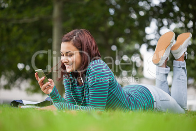 Smiling casual student lying on grass texting