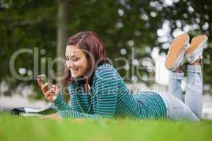 Smiling casual student lying on grass texting