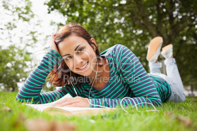 Cheerful casual student lying on grass reading a book