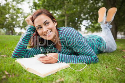 Smiling casual student lying on grass listening to music