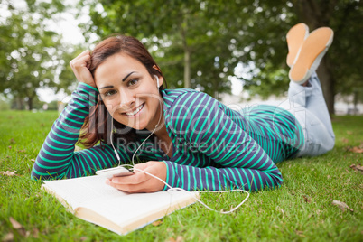 Happy casual student lying on grass listening to music