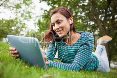 Smiling casual student lying on grass using tablet