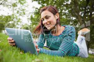 Smiling casual student lying on grass using tablet