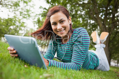 Cheerful casual student lying on grass using tablet