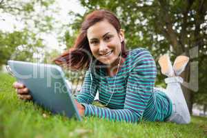 Cheerful casual student lying on grass using tablet