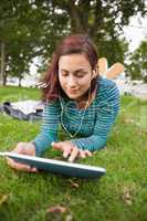 Calm casual student lying on grass using tablet