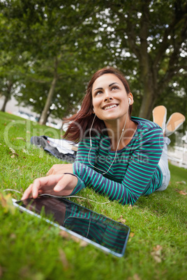 Day dreaming casual student lying on grass using tablet