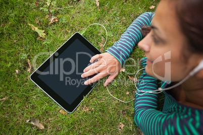 Casual student lying on grass using tablet listening to music