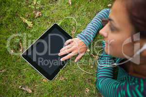 Casual student lying on grass using tablet listening to music