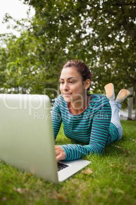 Casual student lying on grass using laptop