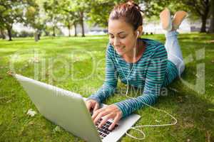 Smiling casual student lying on grass using laptop