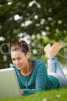 Happy casual student lying on grass using laptop
