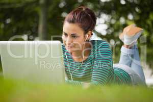 Pretty casual student lying on grass using laptop