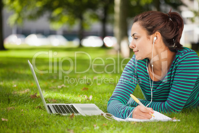 Attractive casual student lying on grass taking notes