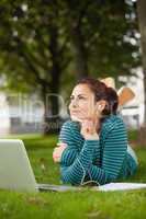 Thoughtful casual student lying on grass taking notes