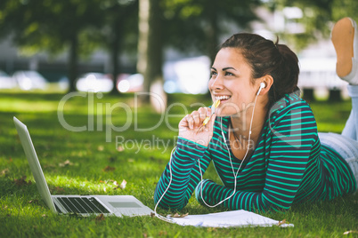 Laughing casual student lying on grass taking notes