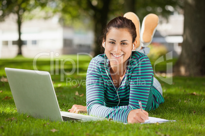 Happy casual student lying on grass taking notes