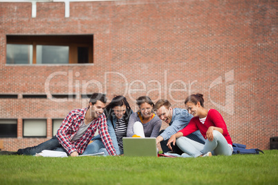 Five casual students sitting on the grass pointing at laptop