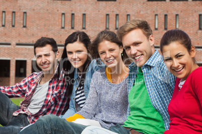 Five students sitting on the grass smiling at camera