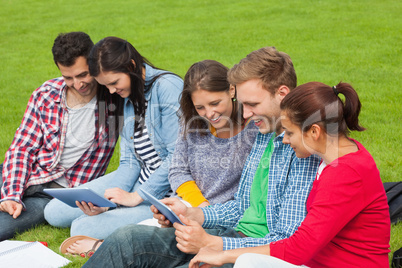 Five students sitting on the grass using tablet