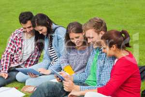 Five students sitting on the grass using tablet