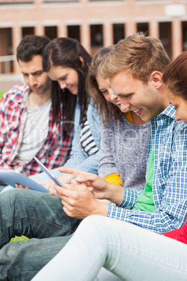 Five casual students sitting on the grass using tablet