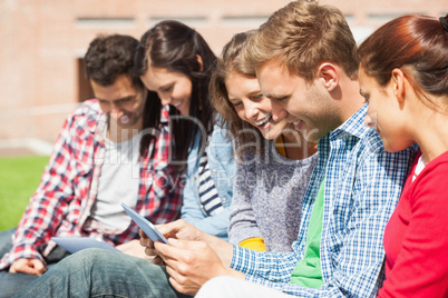 Five smiling students sitting on the grass using tablet