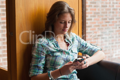 Casual smiling student sitting next to window texting
