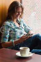 Casual cheerful student sitting next to window texting