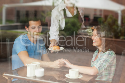 A couple holding hands while waitress serving food