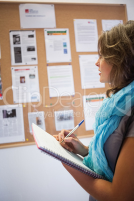 Casual student taking notes in front of notice board