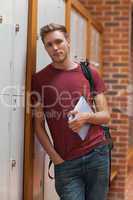 Handsome student leaning against lockers holding tablet