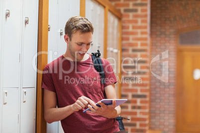 Handsome student leaning against lockers using tablet