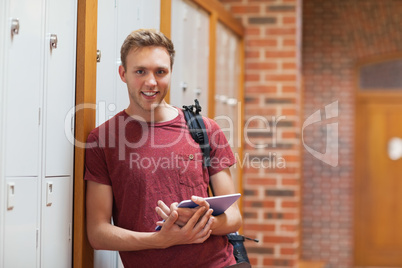 Handsome smiling student leaning against lockers using tablet