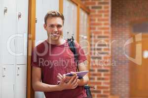 Handsome smiling student leaning against lockers using tablet