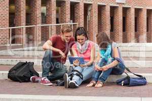 Smiling students sitting on stairs using tablet