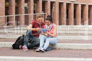 Happy students sitting on stairs using tablet