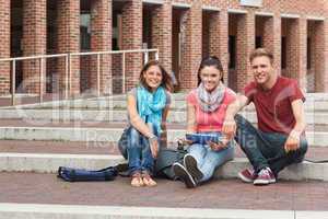 Smiling students sitting on stairs holding tablet