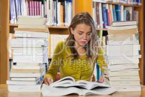 Concentrating pretty student studying between piles of books