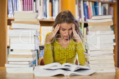 Frustrated pretty student studying between piles of books