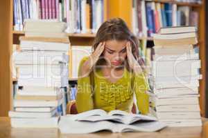 Frustrated pretty student studying between piles of books