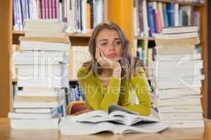 Thoughtful pretty student studying between piles of books